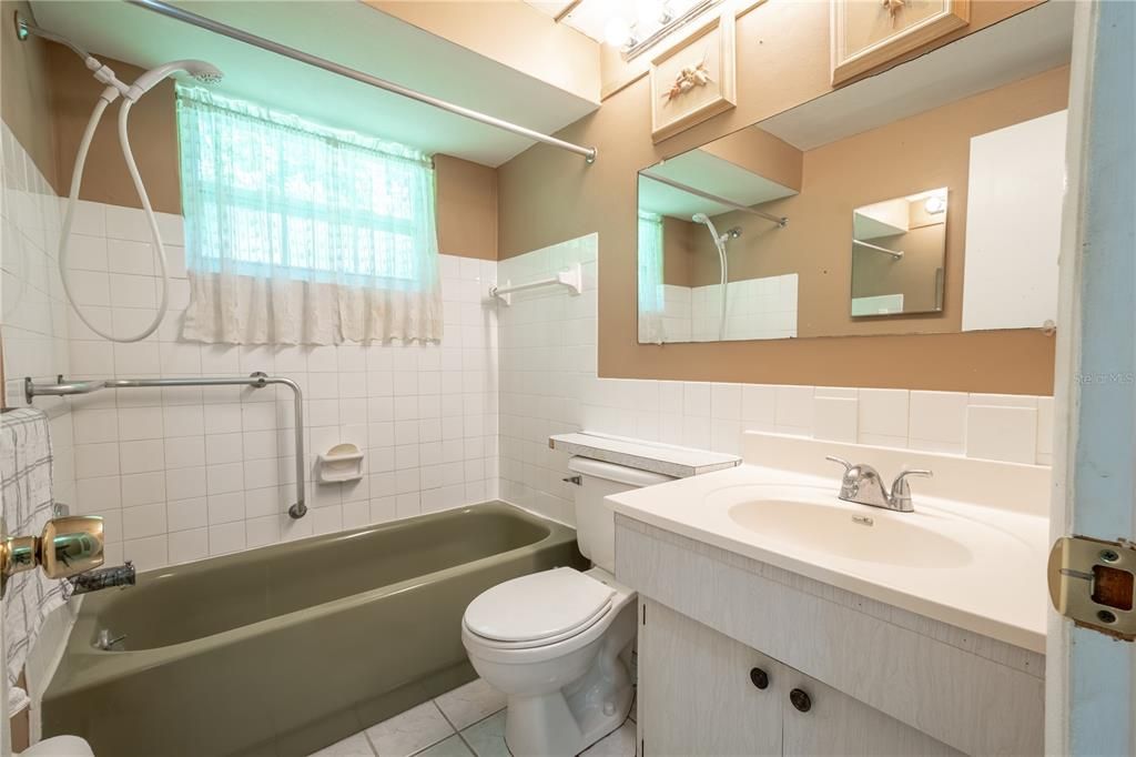 Bathroom 2 features a mirrored sink with storage, a tub with shower and grab bar and a ceramic tile floor.