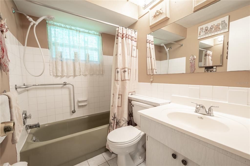 Bathroom 2 features a mirrored sink with storage, a tub with shower and grab bar and a ceramic tile floor.