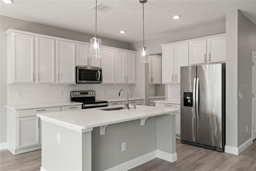 Newly updated kitchen with large center island, 42" cabinets with crown molding, quartz countertops, subway tile backsplash and new Whirlpool stainless steel refrigerator and range.