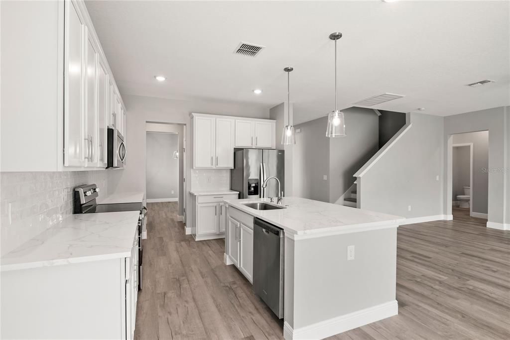 Newly updated kitchen with large center island, 42" cabinets with crown molding, quartz countertops, subway tile backsplash and new Whirlpool stainless steel refrigerator and range.