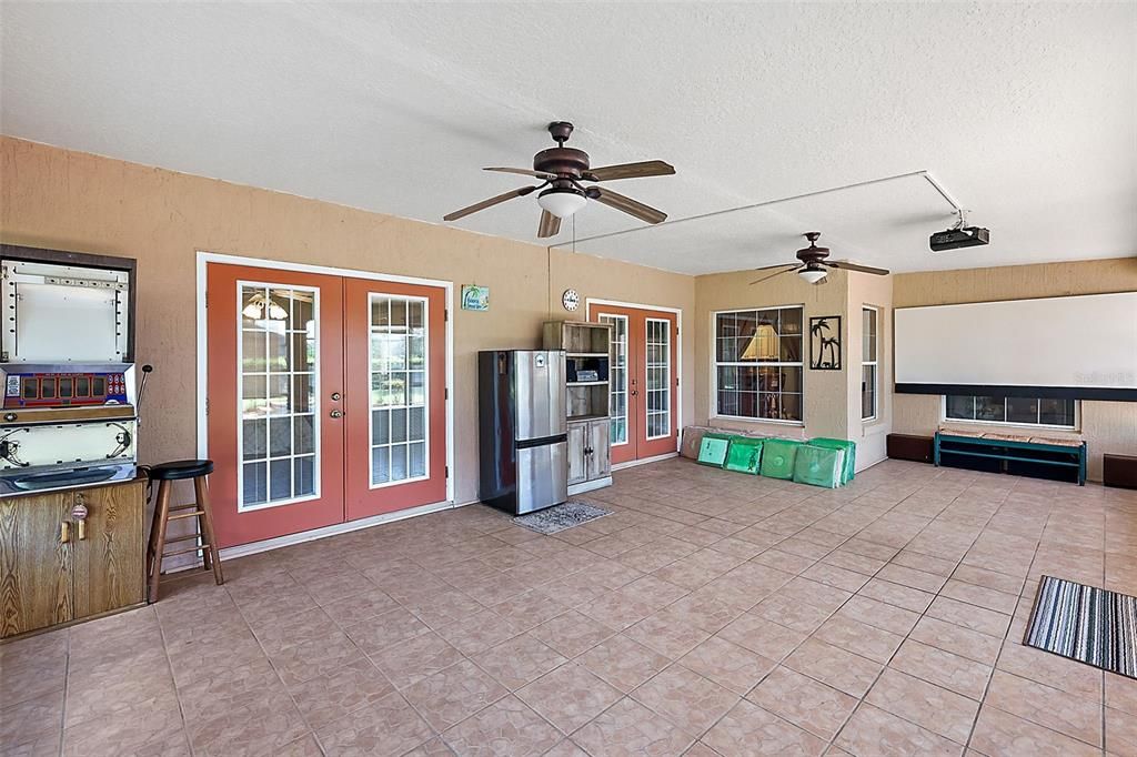 Enclosed lanai/Florida room with tile, fans, French door entry to home, and retractable movie screen with projector