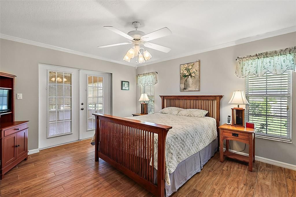 Owner's bedroom with wood floors, crown molding, ceiling fan, and French doors to the lanai/Florida room