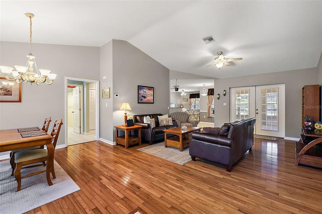 Living room/dining room combo. Vaulted ceilings, real wood floors, French doors lead to the lanai/enclosed Florida room