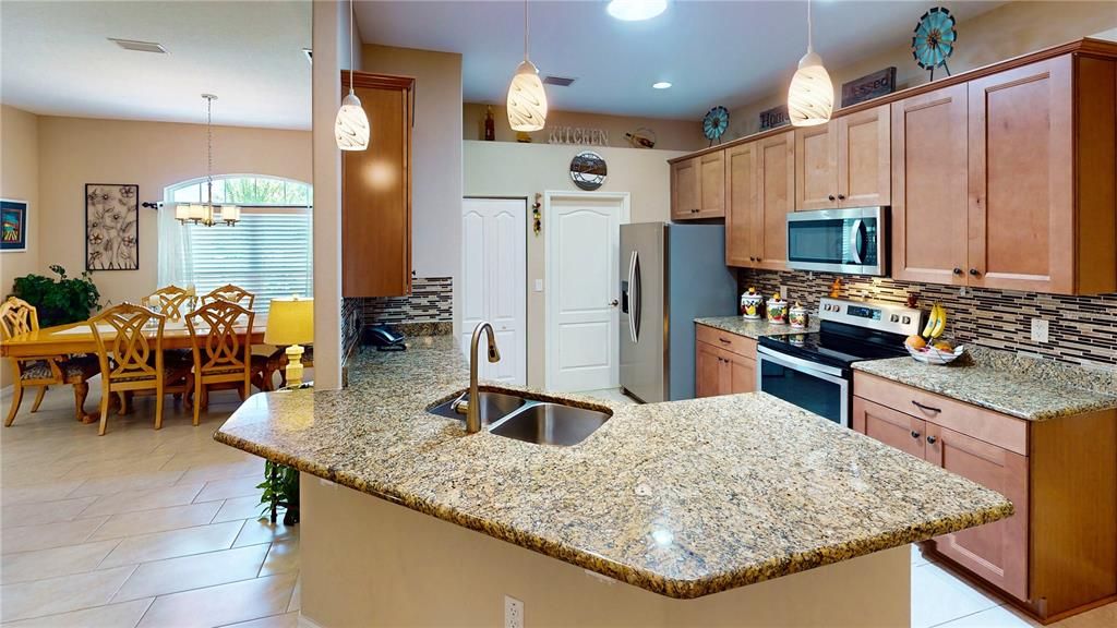 The kitchen features granite counters, an overhanging breakfast bar, rich wood cabinetry, a stunning backsplash, all stainless steel appliances, recessed lighting, and a pantry for ample storage.