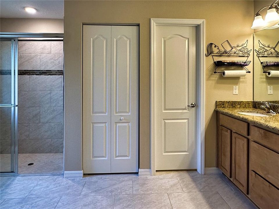 The master bath is a spa-like oasis, featuring a private water closet, a spacious walk-in shower, and rich wood cabinetry with double undermount sinks. Natural light streams through the window, highlighting the elegant tile floors and creating a serene ambiance for your daily routine.