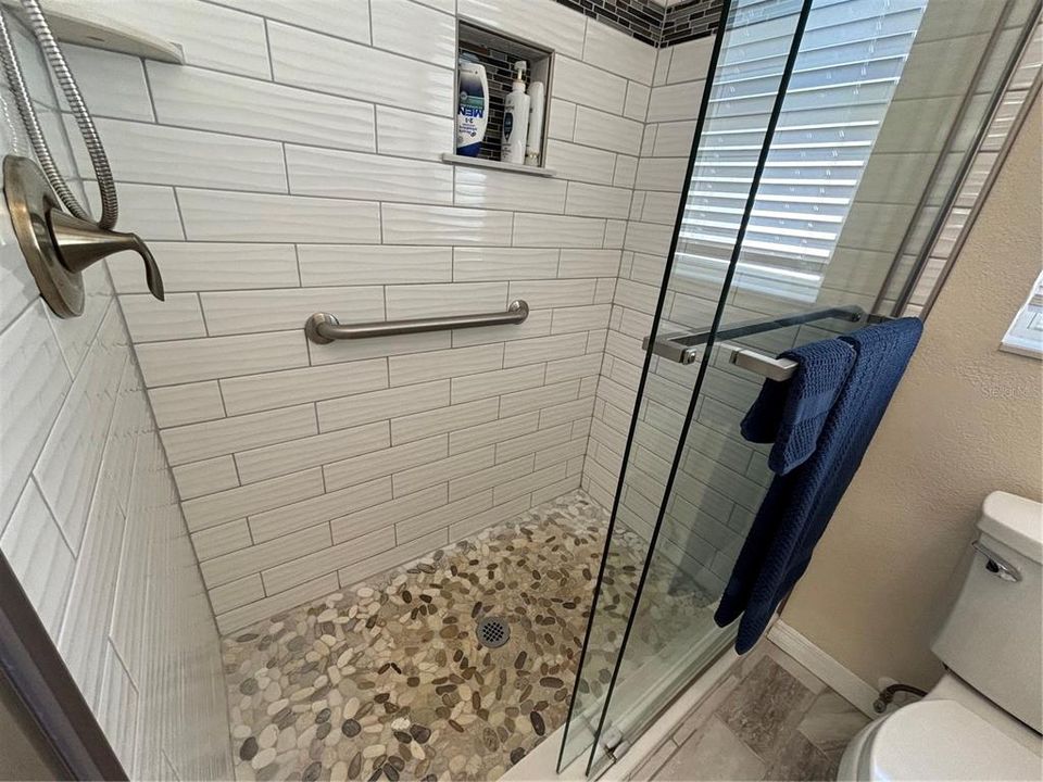 Shower riverstone, doors shampoo niche, grab bar, window, tile