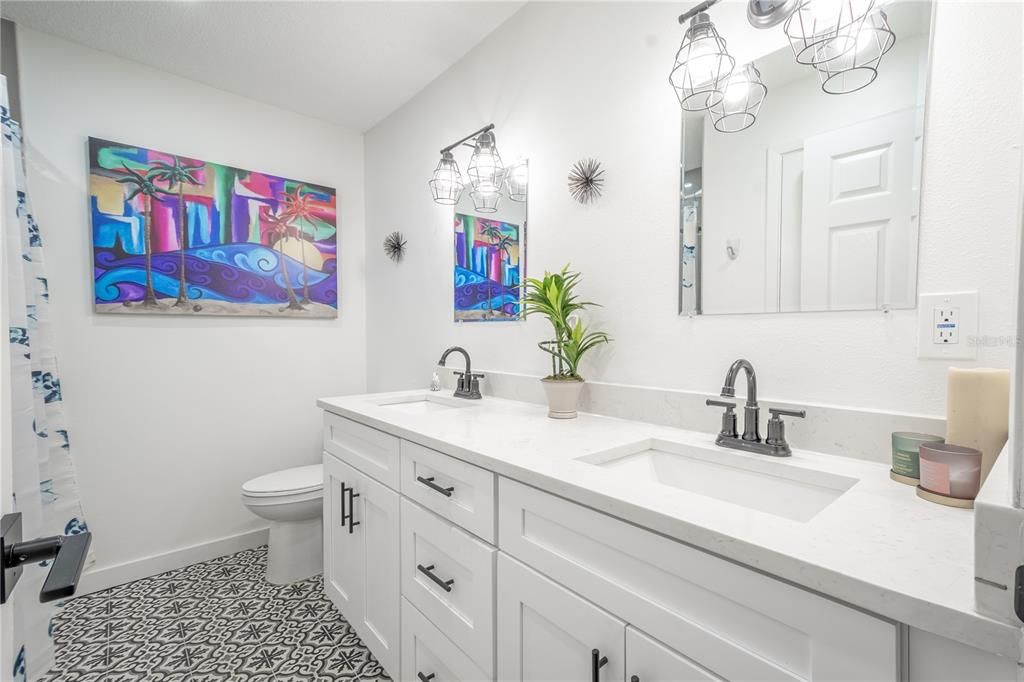 Bathroom 2 features a mirrored, dual sink vanity with dpwn light fixtures and quartz countertops.