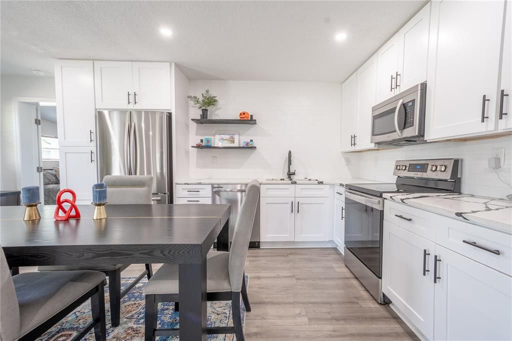 The kitchen features quartz countertops, an abundance of cabinets, tile backsplash and floating shelves.