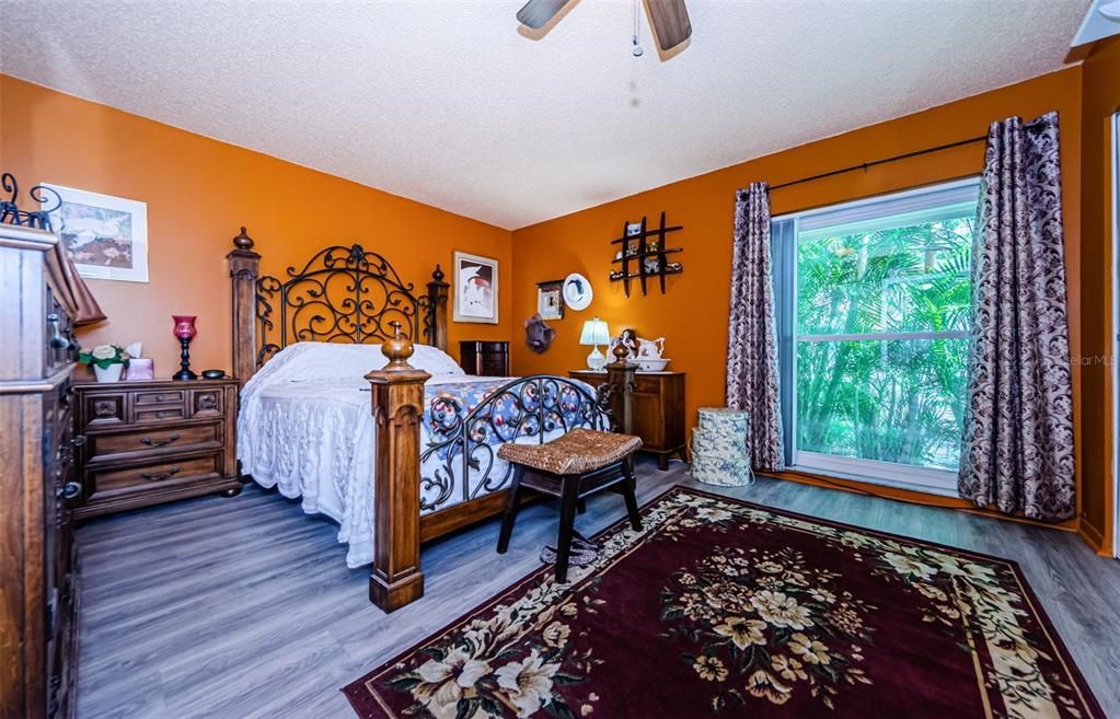 Master bedroom with luxury vinyl flooring has a double pane window looking out to beautiful landscaping