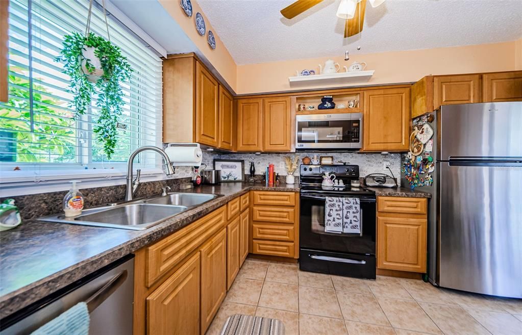 Kitchen features wood cabinets, decorative tile backsplash, newer window over double sink with ceramic tile