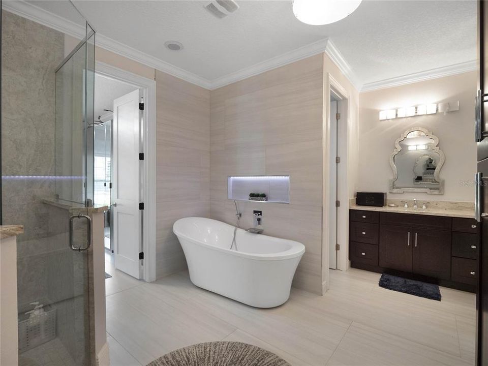 Primary bathroom featuring separate vanity areas and spacious shower and soaking tub leads in to the custom built in closet.