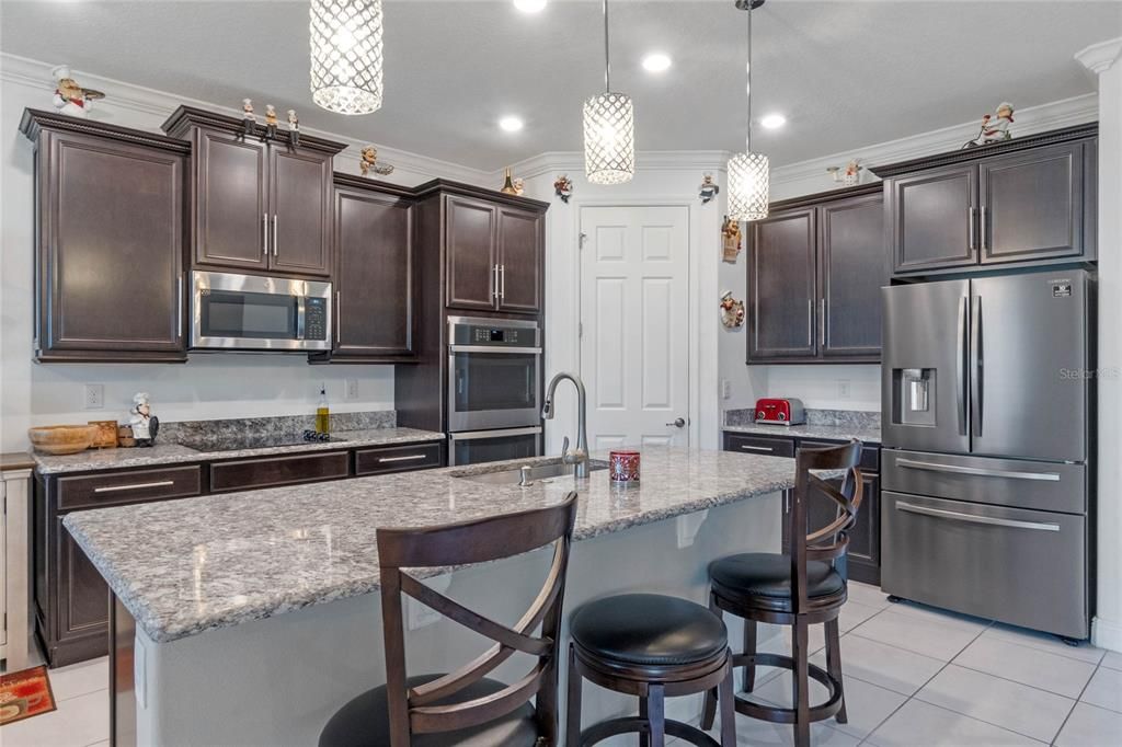 The elegant granite island with bar seating serves as the heart of the kitchen, offering a perfect spot for casual dining, meal prep, and socializing with guests.