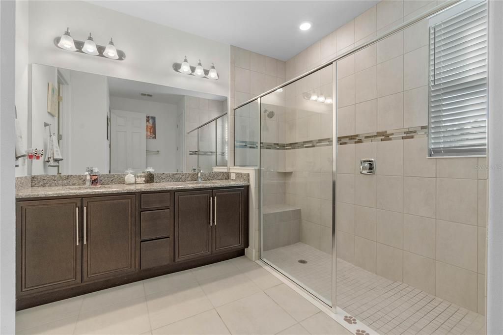 The primary ensuite bathroom boasts dual vanities with granite countertops and a luxurious seamless glass shower adorned with tile, combining elegance with functionality.