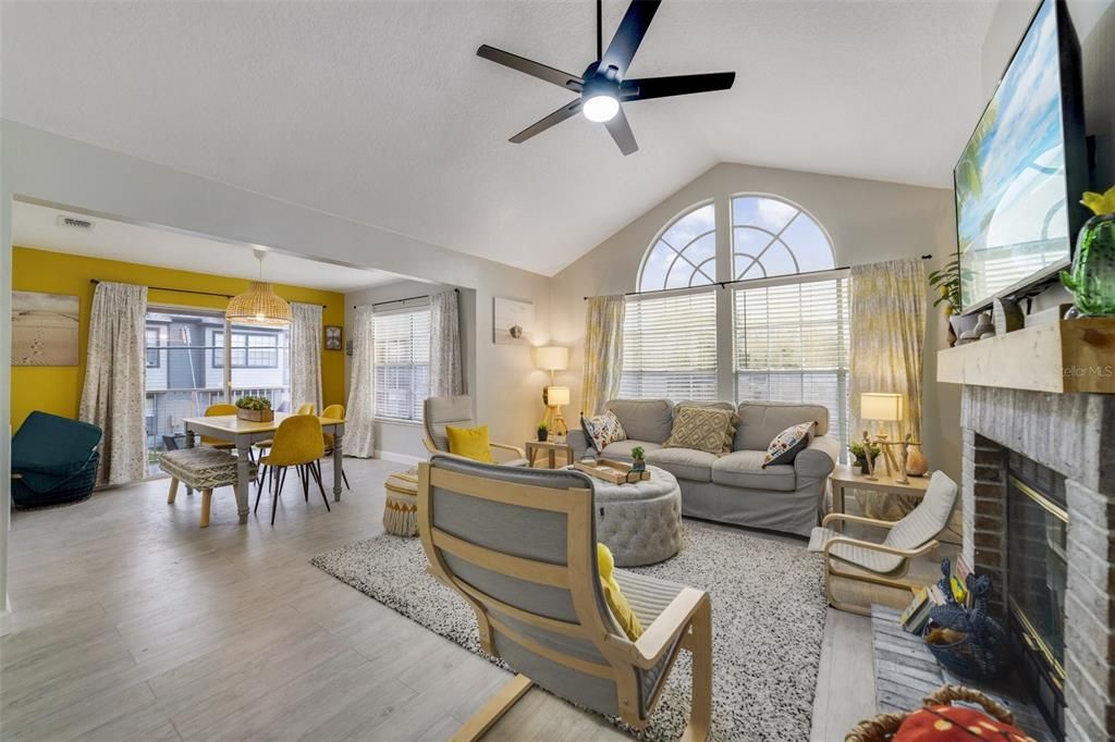 Natural light flows through the windows and reflects off the soaring ceilings and cheery color palette in the spacious main living area showcasing a lovely FIREPLACE with a BRICK SURROUND, making this a wonderful space to entertain guests.