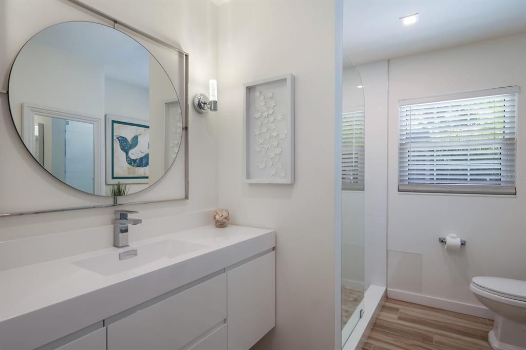 The delightfully renovated guest bathroom features a floating vanity, with a sleek counter-top and sink, and open concept glass shower.