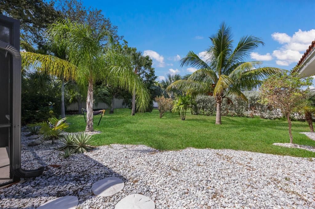 The tropically landscaped yard boasts several palm trees, a luscious lawn, and shelled garden spaces.