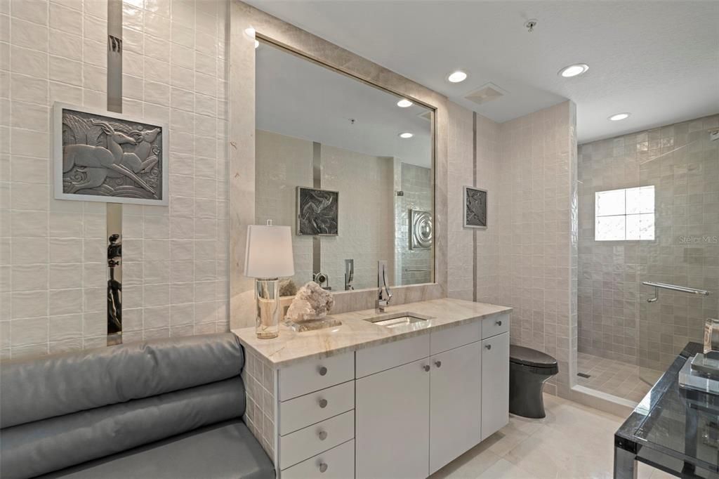 Ensuite guest bath with Taj Mahal Quartzite and sea glass counters, high seat Kohler commodes, glass sink, shower niches, and Riobel shower handles.