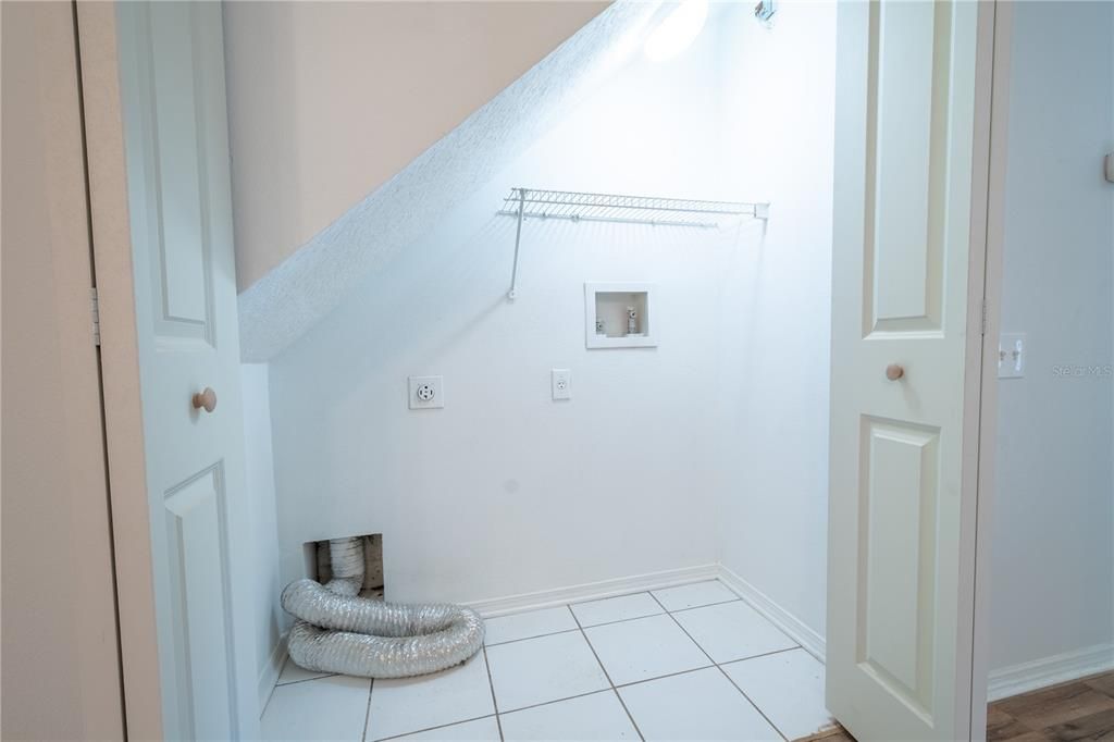 Under stairs laundry room features hook-ups for washer and fryer, a shelf and ceramic tile floor.