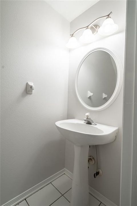 The 1st floor half bath features a pedestal sink with mirror and downlight fixture.