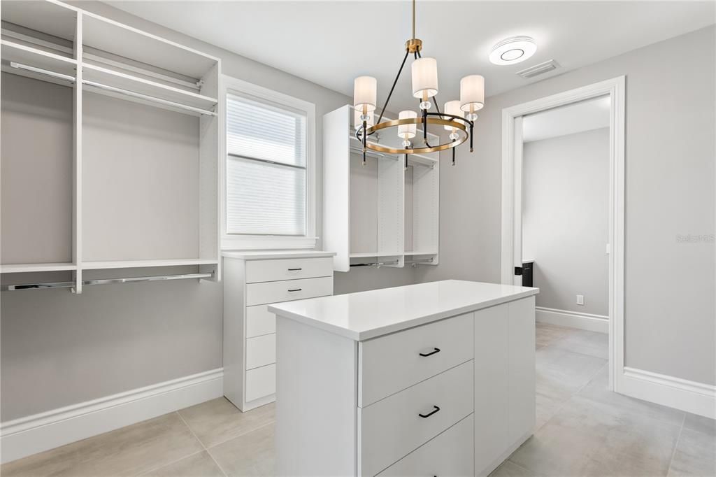 Primary en suite Walk through dressing Closet with built in shelves and center island dresser adjacent to en suite bath and laundry