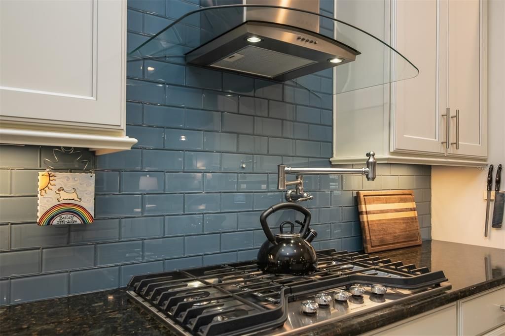 A handy pot filler, the 5 burner gas cooktop, glass tile backsplash, and designer range hood make this a true chef's delight kitchen.