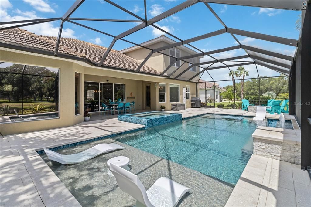 The pool area features a sun shelf for lounging under the sun, complemented by a tranquil waterfall and an infinity edge spa for ultimate relaxation. Outdoor shower with hot water to rinse off after a swim is true Florida Paradise living.