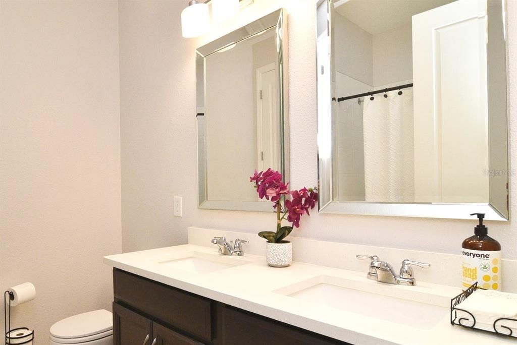 Secondary Bath between Bedrooms 2 & 3: double-sink vanity with quartz counter; decorative mirrors and lights; tub/shower combo; ceramic tile floor