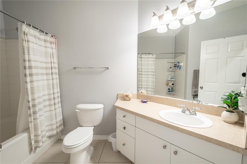 Bathroom 2  features a ceramic tile floor, a tub with shower, and a mirrored vanity with storage and down light fixture.