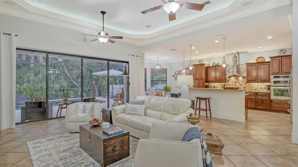 Spacious great room featuring tray ceilings, 16" tile floors, custom built-ins, and a pocket sliding door that opens up to the screened-in lanai.