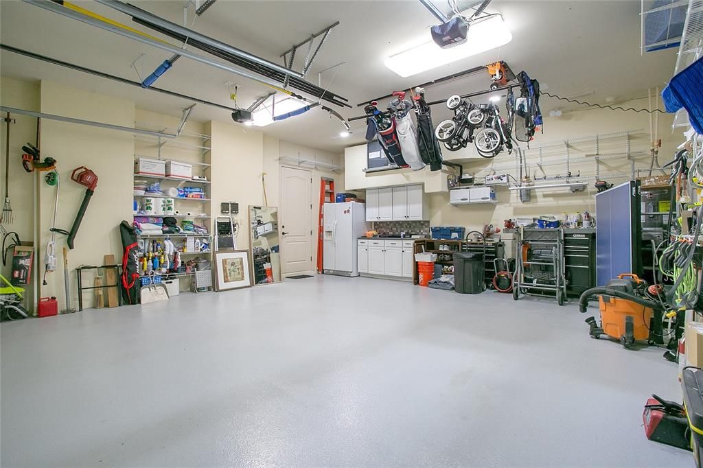 Garage features epoxy flooring, extra refrigerator, and storage cabinets