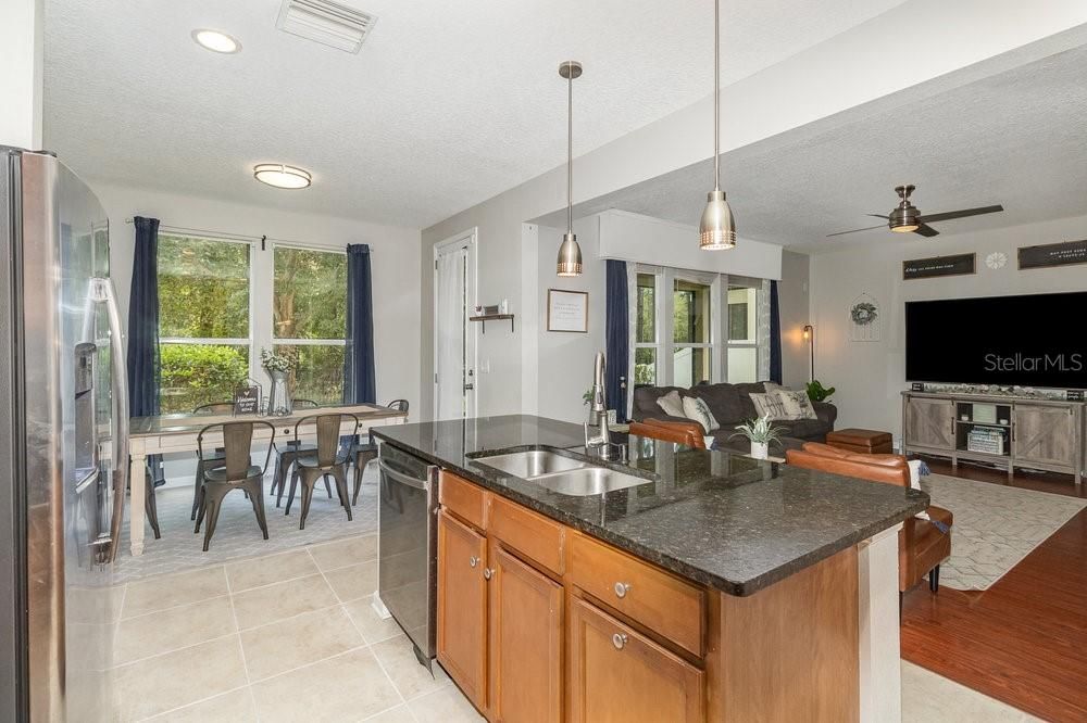 Open concept Kitchen with Granite counters and breakfast bar with Pendent lighting, Stainless Steel appliances, recessed lighting, dinette and tiled flooring.