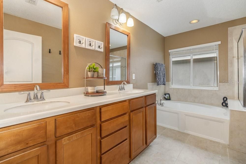 Primary Bathroom with dual sinks, Corian counters, Garden tub with separate shower stall, and tiled flooring.