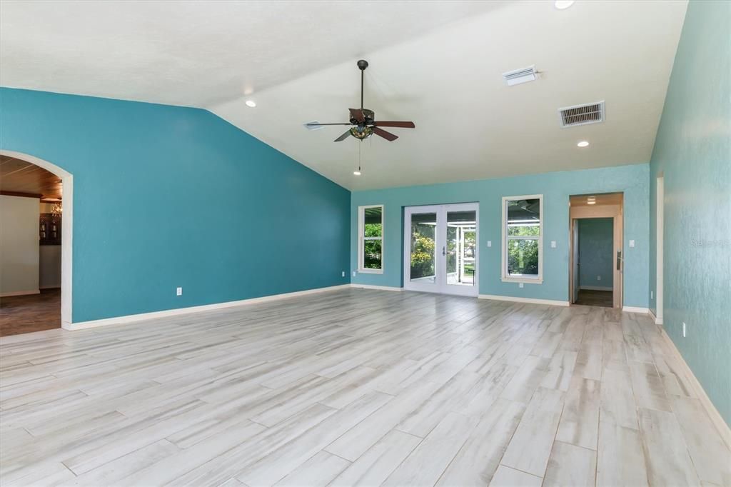 Living/Great Room from front to back view. French doors provide access to wrap-around screened lanai. Primary Bedroom located at rear. Arched opening leads to Kitchen/Dining area.