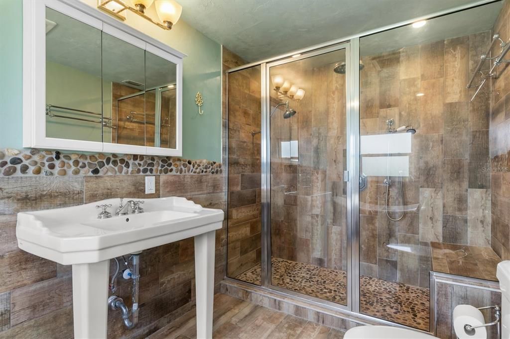 Huge floor-to-ceiling tiled shower with multiple shower heads and convenient bench.