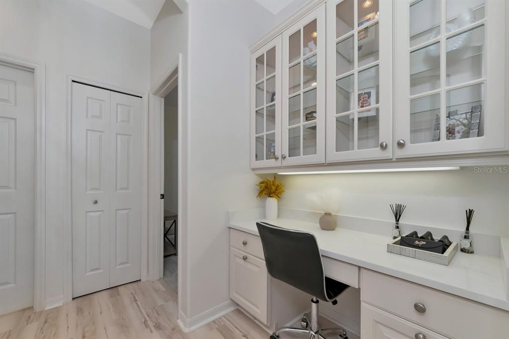 Built-in desk just off the kitchen with glass cabinets and lighting.