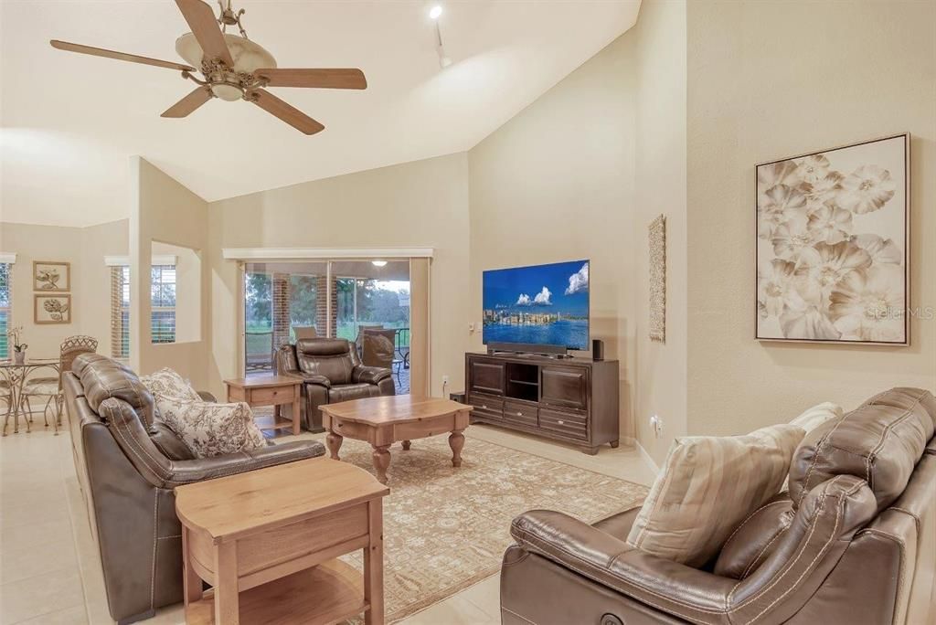 Living room featuring vaulted ceilings, ceramic tile, and sliding glass doors to the covered screened-in lanai.