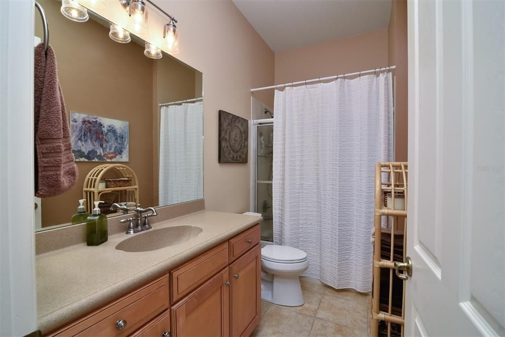 The guest bath is next to the guest bedrooms and has a combination shower/tub, elevated maple vanity with cultured top, elongated stool, and glass shower door.