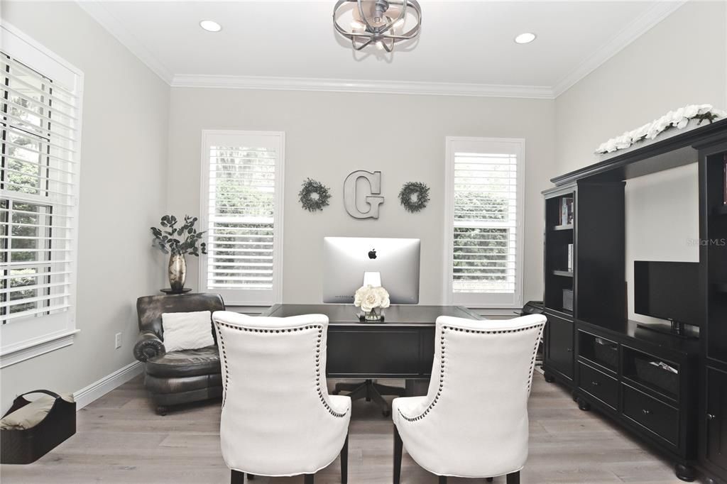 First-floor office with wide-plank wood flooring, large windows with plantation shutters, crown molding and double glass doors.