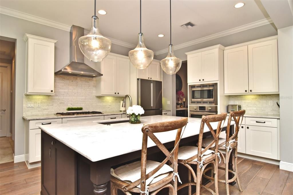 Gourmet kitchen with wide-plank wood flooring, crown molding, large center island with large undermount stainless-steel sink, and Restoration Hardware pendant lights