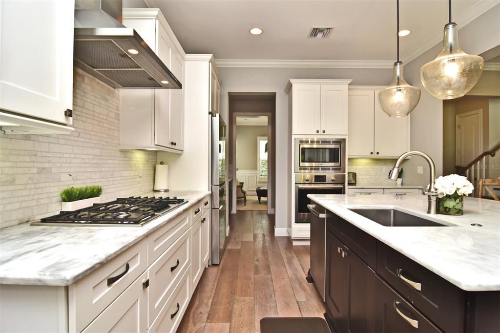 Wide-plank wood flooring, 42" white upper cabinets, quartzite countertops, under cabinet lighting, and Bosch appliances in kitchen