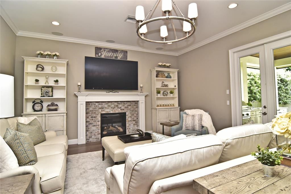 Great room with wide-plank wood flooring, gas fireplace, decorative ceiling fixture, and crown molding