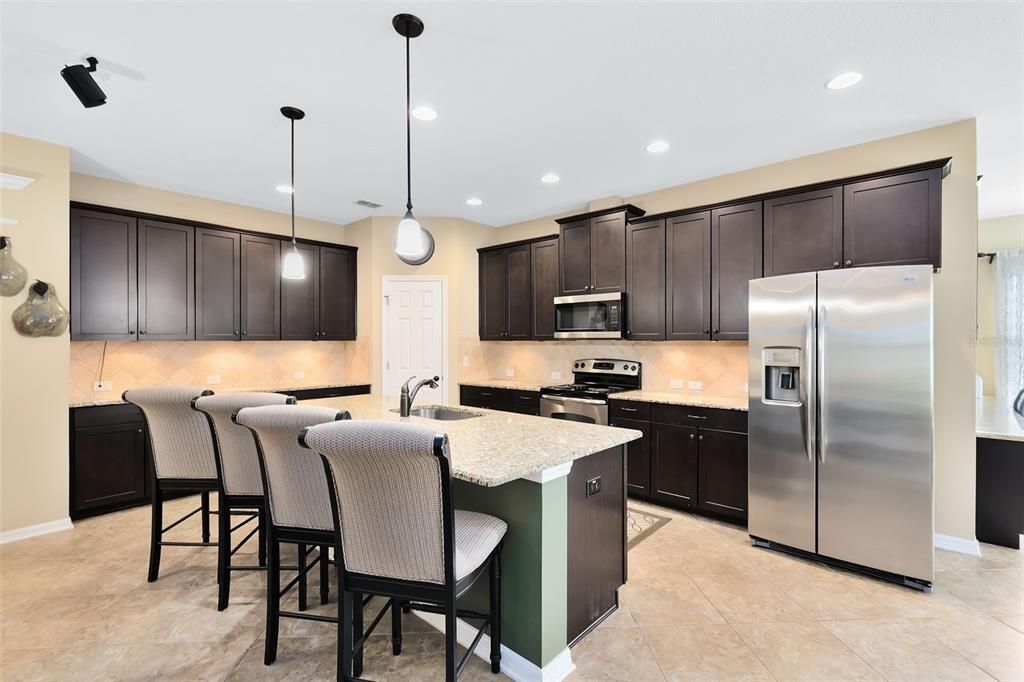 The kitchen is a chef’s dream, featuring under-cabinet lighting, a granite-topped breakfast bar and counters, stainless steel appliances, and a stylish tile backsplash.