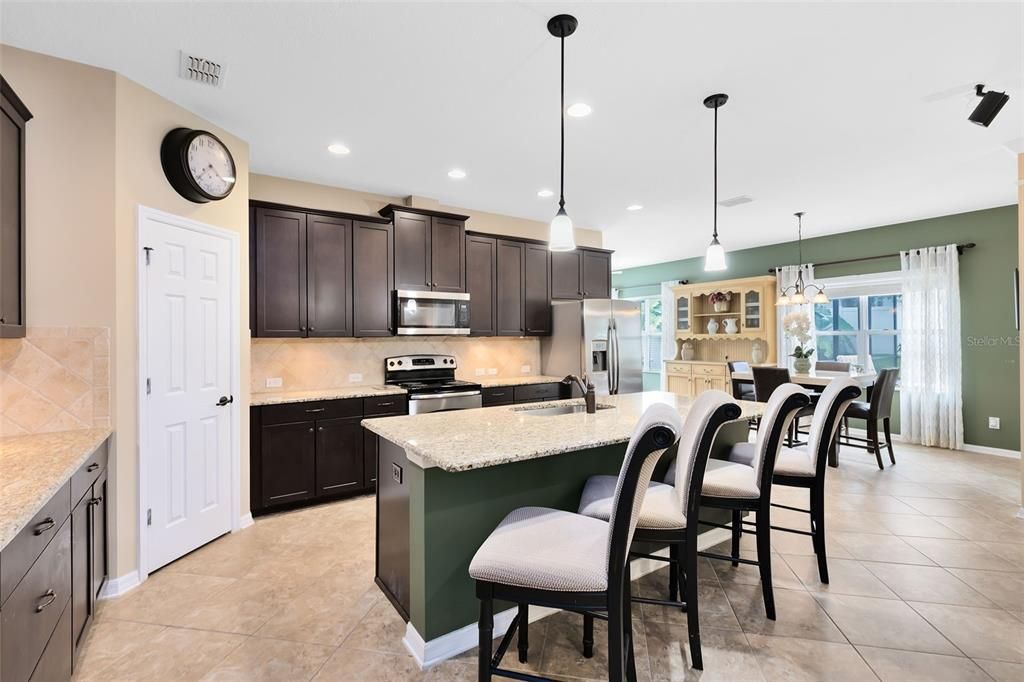 The kitchen is a chef’s dream, featuring under-cabinet lighting, a granite-topped breakfast bar and counters, stainless steel appliances, and a stylish tile backsplash.