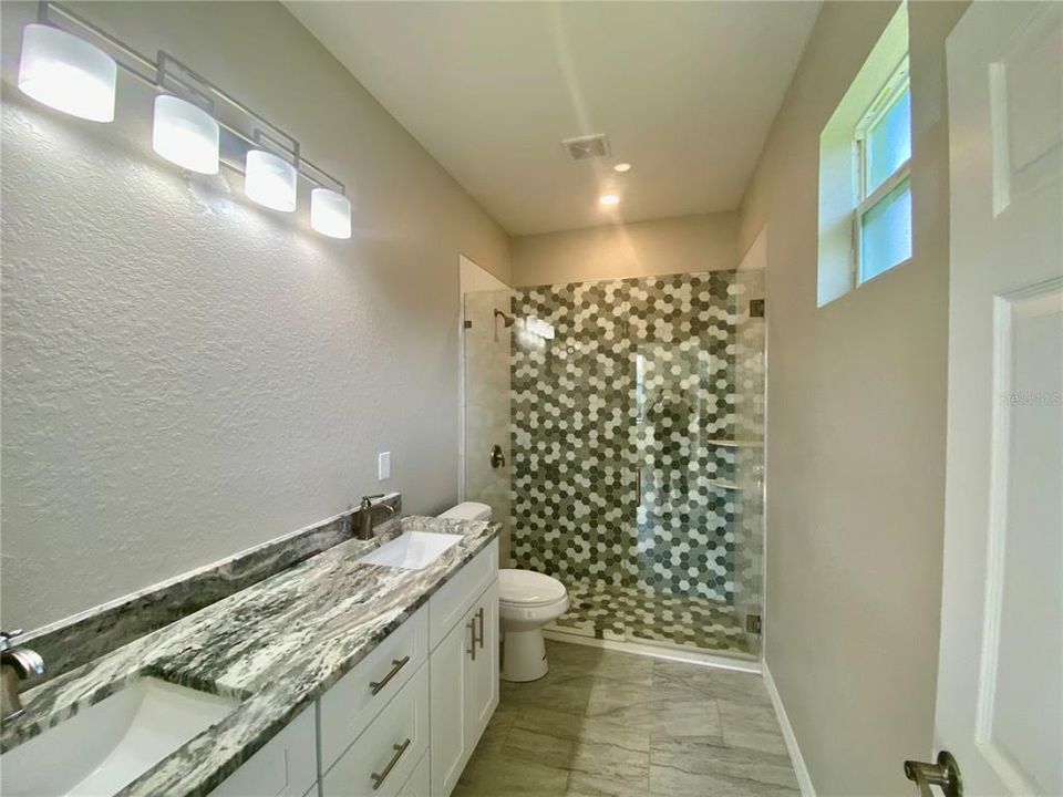 primary bath with double vanity, granite, tiled walk-in shower with glass shower door.