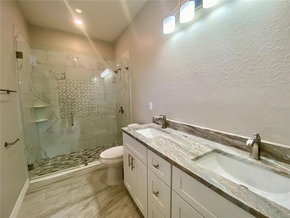 master bath with double vanity & granite counter tops & tiled walk-in shower with glass shower door.