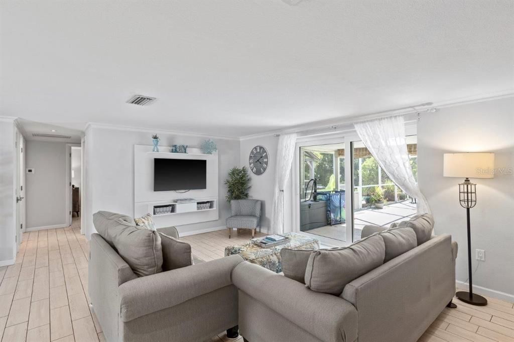 Large great room featuring crown molding, wood plank tile flooring, and glass doors leading out to the screened-in lanai and hot tub.