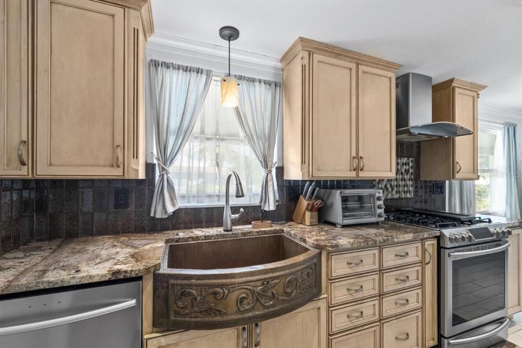 Gourmet kitchen featuring granite counters, custom wood cabinets, stainless steel appliances, and hammered copper farm sink.