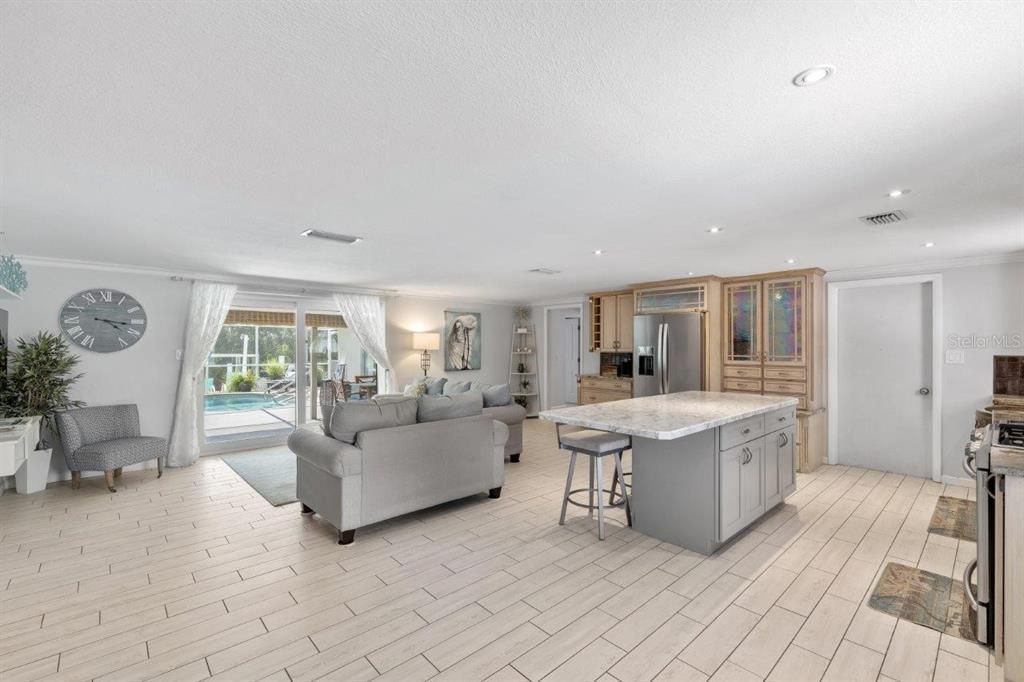 Large great room featuring crown molding, wood plank tile flooring, and glass doors leading out to the screened-in lanai and hot tub.