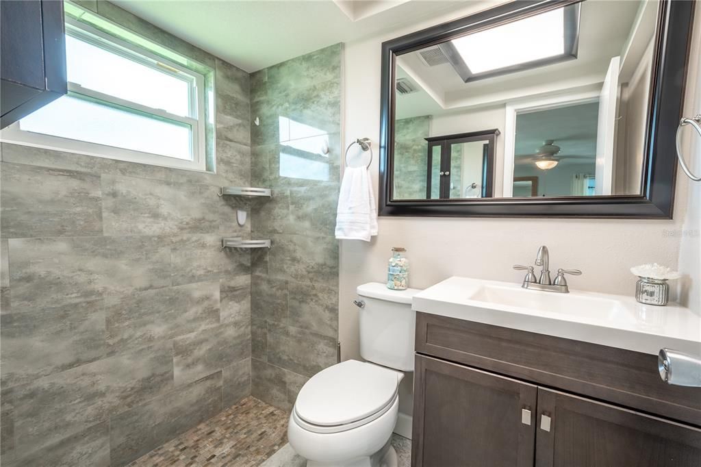 The primary bath features an beautifully tiled walk-in shower, a mirrored vanity with storage and ceramic tile floor.