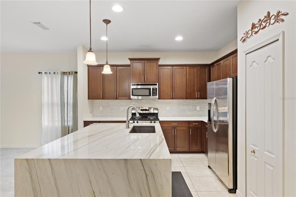 Gourmet kitchen featuring quartz counter tops, ample cabinetry, a large island with waterfall edge, and stainless steel appliances.